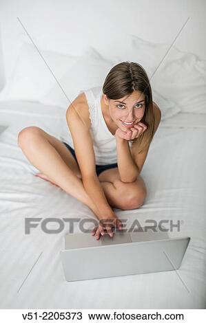 Stock Image - Young pretty woman with laptop in bed. Fotosearch