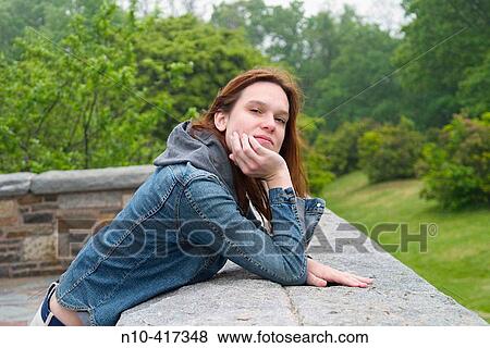 Stock Photo - Young redhead woman leaning on a concrete ledge at a park.. Fotosearch