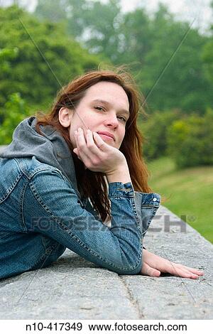 Stock Photo - Young redhead woman leaning on a concrete ledge at a park.. Fotosearch