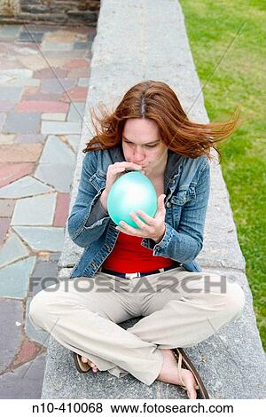 Young redhead woman sitting on a stone ledge at a park in Connecticut, USA, blowing up a balloon. View Large Photo Image Stock Photo - Young redhead woman sitting on a stone ledge at a park in Connecticut, USA, blowing up a balloon.. Fotosearch