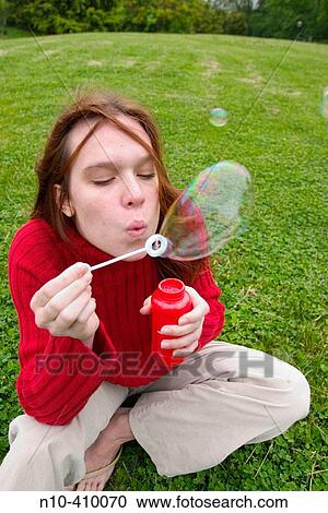 Young redhead woman sitting on the grass at a park in Connecticut, USA, blowing soap bubbles. View Large Photo Image Stock Image - Young redhead woman sitting on the grass at a park in Connecticut, USA, blowing soap bubbles.. Fotosearch