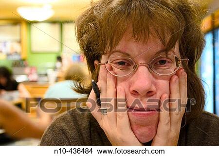 Young redhead woman, wearing glasses, sitting at a table in a cafe, with her head resting on her hands. View Large Photo Image Picture - Young redhead woman, wearing glasses, sitting at a table in a cafe, with her head resting on her hands.. Fotosearch