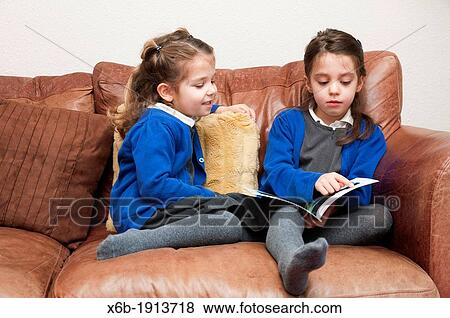 Stock Photo - Young sisters in Primary School uniform reading a book together. Fotosearch