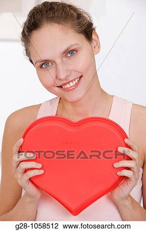 Stock Image - young smiling happy woman holding a red heart in front of her. Fotosearch