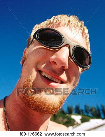 Stock Image - Young smiling male face wide angle against blue sky. Fotosearch