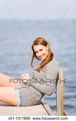Young smiling woman enjoying a coffee relaxing and sitting on a pier View Large Photo Image Stock Image - Young smiling woman enjoying a coffee relaxing and sitting on a pier. Fotosearch