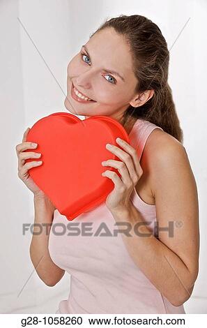 Stock Image - young smiling woman holding a red heart in front of her. Fotosearch