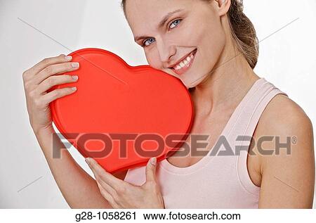 young smiling woman holding a red heart in front of her View Large Photo Image Stock Image - young smiling woman holding a red heart in front of her. Fotosearch
