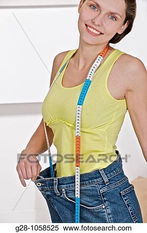 young smiling woman holding her too large jeans after slimming, dieting, with a measuring tape around her neck, looking at camera View Large Photo Image Stock Photography - young smiling woman holding her too large jeans after slimming, dieting, with a measuring tape around her neck, looking at camera. Fotosearch