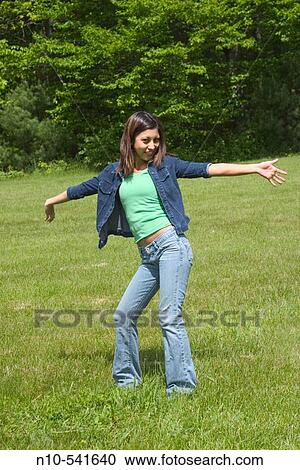 Stock Image - Young Spanish/Asian woman dancing alone at a park.. Fotosearch