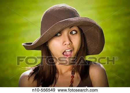 Stock Photo - Young Spanish/Asian woman, wearing a hat, posing at a park.. Fotosearch