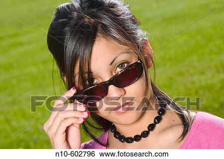 Young Spanish/Asian woman, wearing sunglasses, posing at a park View Large Photo Image Stock Photograph - Young Spanish/Asian woman, wearing sunglasses, posing at a park. Fotosearch