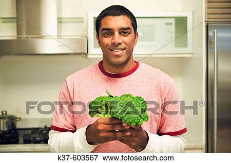 Young Sri Lancan 20-30 y/o man in modern kitchen holding bunch of brocolli. View Large Photo Image Stock Photo - Young Sri Lancan 20-30 y/o man in modern kitchen holding bunch of brocolli.. Fotosearch