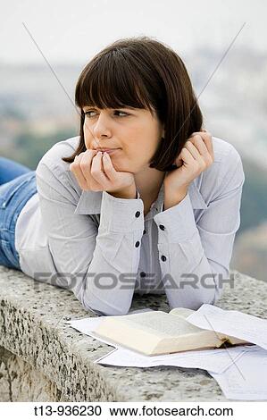 Young student woman is lying outdoors with a book and papers before her View Large Photo Image Stock Image - Young student woman is lying outdoors with a book and papers before her. Fotosearch