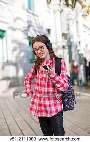 Stock Image - Young stundent girl with bag going to school with earphones. Fotosearch
