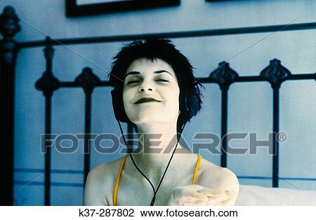 Stock Image - Young teenage woman listening to music on headphones. Fotosearch