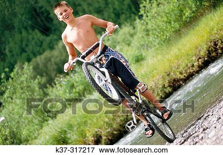 Young teenage youth wearing swimming trunks, balancing on back wheel of his mountain bike View Large Photo Image Stock Photo - Young teenage youth wearing swimming trunks, balancing on back wheel of his mountain bike. Fotosearch