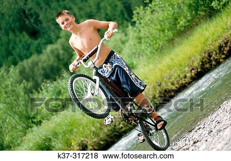 Young teenage youth wearing swimming trunks, balancing on back wheel of his mountain bike View Large Photo Image Stock Photo - Young teenage youth wearing swimming trunks, balancing on back wheel of his mountain bike. Fotosearch