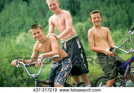 Stock Photo - Young teenage youths on mountain bikes, wearing swimming trunks. Fotosearch