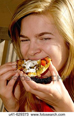 Stock Image - Young teenager trying to look gracefull eating a pizza.. Fotosearch