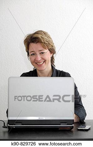 Young urban causcasian woman smiling into the camera while sitting in front of her Laptop, having her iphone besides her, Hamburg, Germany, Europe View Large Photo Image Stock Photograph - Young urban causcasian woman smiling into the camera while sitting in front of her Laptop, having her iphone besides her, Hamburg, Germany, Europe. Fotosearch