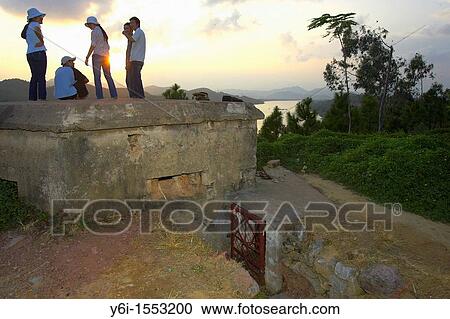 Stock Image - Young visitors view Perfume River sunset on American bunker Vong Canh Hill Hue central Vietnam. Fotosearch