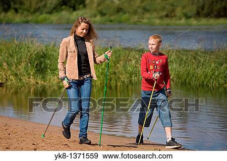 Stock Photo - Young woman and teenage boy doing nordic walking by river water. Fotosearch