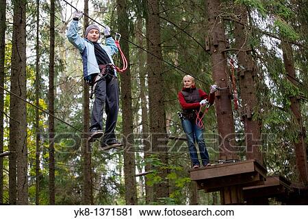 Stock Image - Young woman and teenage boy on zip wire in adventure park trail in Otep??, Estonia. Fotosearch