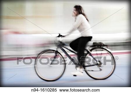Stock Photography - Young woman biking through the city.. Fotosearch