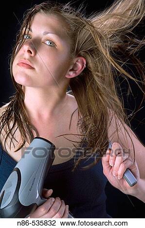 Stock Image - Young woman blow drying her hair. Fotosearch