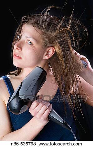 Stock Photo - Young woman blow drying her hair. Fotosearch