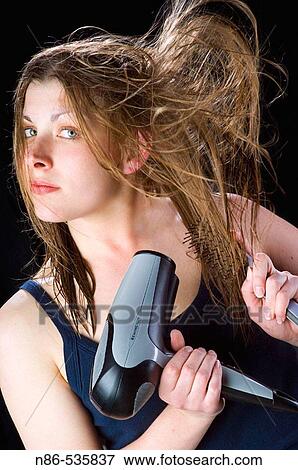 Young woman blow drying her hair View Large Photo Image Stock Photo - Young woman blow drying her hair. Fotosearch