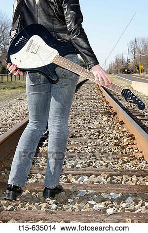 Young woman carrying a guitar standing on railroads looking into and thinking about future View Large Photo Image Picture - Young woman carrying a guitar standing on railroads looking into and thinking about future. Fotosearch