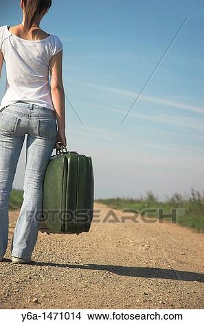 Young woman carrying suitcases on country road, rear view View Large Photo Image Picture - Young woman carrying suitcases on country road, rear view. Fotosearch