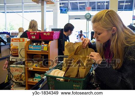 Young woman checking out at cash register in american supermarket View Large Photo Image Stock Photo - Young woman checking out at cash register in american supermarket. Fotosearch