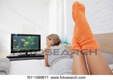 Stock Photo - Young woman chilling out on her bed watching TV. Fotosearch