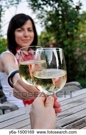 Stock Photo - Young woman clinking glasses with friend in outdoor restaurant. Fotosearch