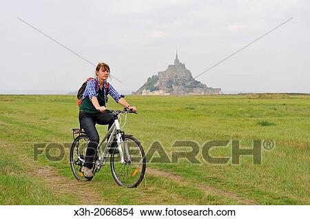 Picture - young woman cycling in the bay of Mont Saint-Michel, Manche department, Low Normandy region, France, Europe.. Fotosearch