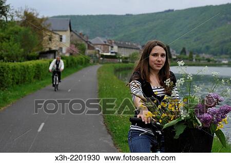 Stock Image - young woman cycling on cycle lane along the Meuse River at Haybes, Ardennes department, Champagne-Ardenne region of northeasthern France, Europe.. Fotosearch