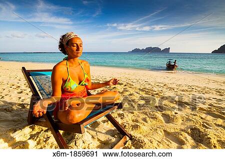 Stock Image - Young woman doing yoga on a deckchair Long beach Phi Phi Don island Krabi province, Andaman Sea, Thailand. Fotosearch