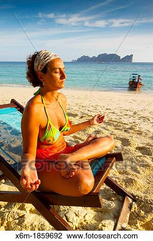 Stock Image - Young woman doing yoga on a deckchair Long beach Phi Phi Don island Krabi province, Andaman Sea, Thailand. Fotosearch