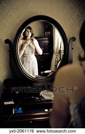 Stock Photo - Young woman dressing in front of a vanity mirror.. Fotosearch