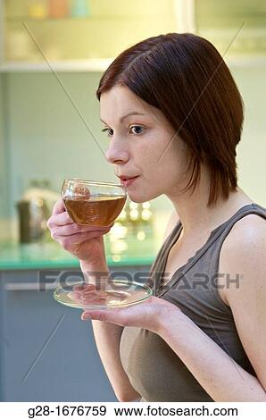 Stock Photo - Young woman drinking a cup of tea in her kitchen. Fotosearch