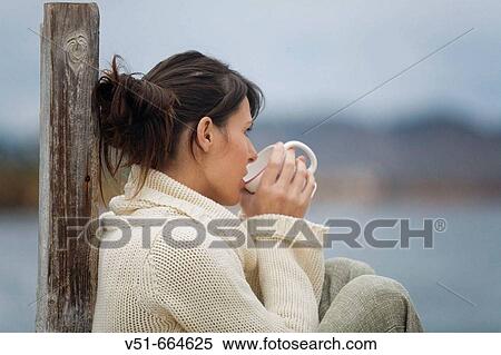 Stock Photography - Young woman drinking herbal infusions looking to the sea.. Fotosearch