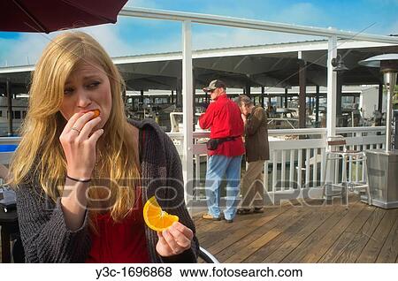 Young woman eating orange slices at a marina with people and yachts in the background View Large Photo Image Stock Photo - Young woman eating orange slices at a marina with people and yachts in the background. Fotosearch