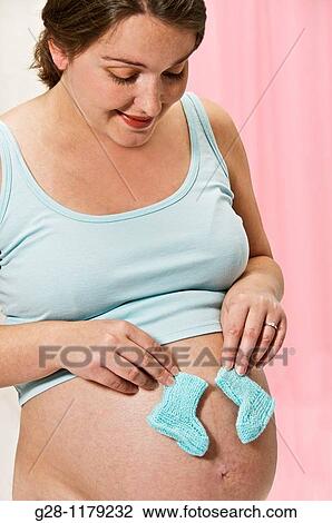 young woman expecting a baby in blue, holding two knitted baby shoes on her stomach View Large Photo Image Stock Image - young woman expecting a baby in blue, holding two knitted baby shoes on her stomach. Fotosearch