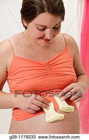 young woman expecting a baby in orange, holding two knitted baby shoes on her stomach View Large Photo Image Stock Image - young woman expecting a baby in orange, holding two knitted baby shoes on her stomach. Fotosearch