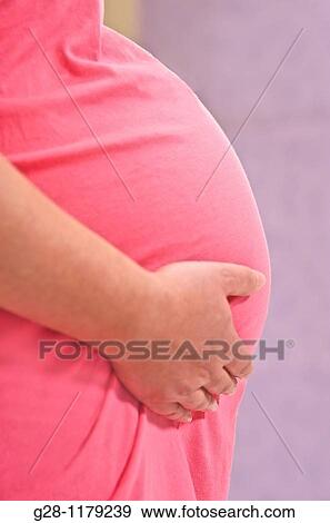 Young woman expecting a baby in pink dress, holding her belly View Large Photo Image Stock Photo - Young woman expecting a baby in pink dress, holding her belly. Fotosearch