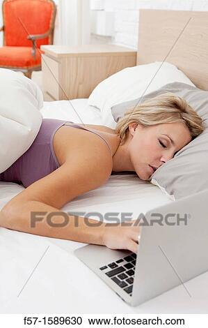 Stock Image - Young woman fallen asleep while on her laptop. Fotosearch