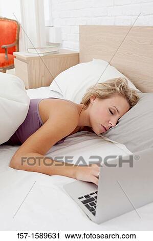 Stock Image - Young woman fallen asleep while on her laptop. Fotosearch